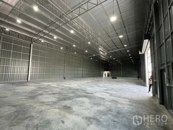 Warehouse for rent in Pak Kret, Nonthaburi - High-clearance warehouse floor with multiple LED lights and metal wall panels.