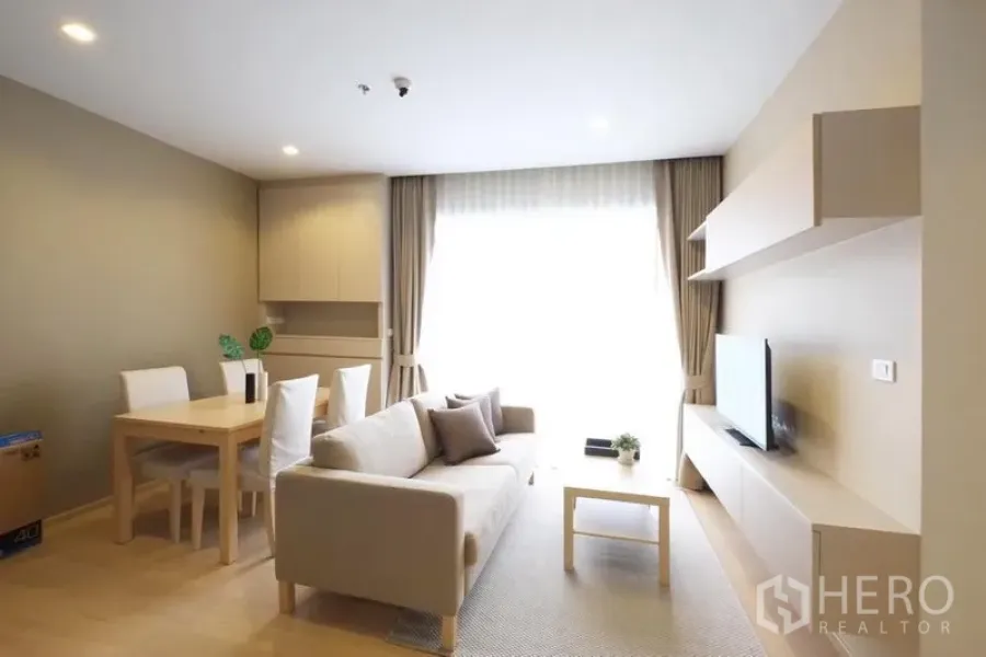 Condominium for rent in Watthana, Bangkok - Open-plan living and dining room with sofa, TV wall unit and four-seat dining table.