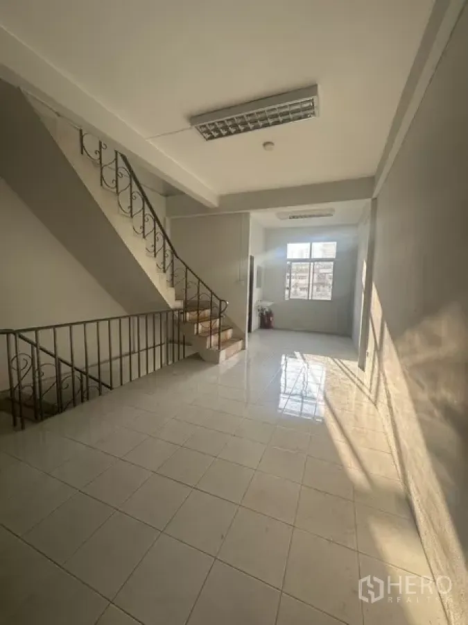 Shophouse for rent in Khlong Toei, Bangkok - Bright tiled landing with metal staircase and sunlit window in a shophouse.