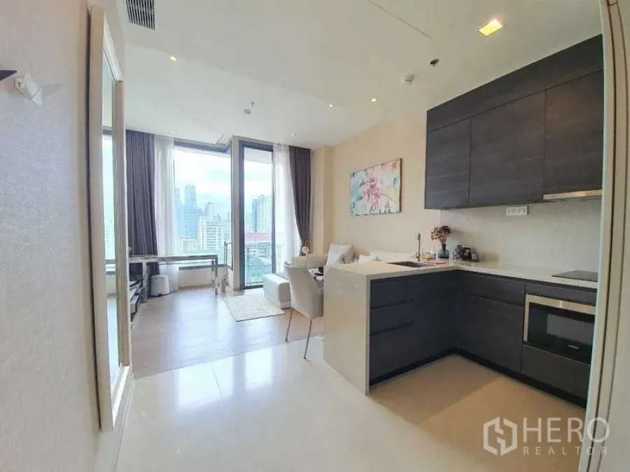 Condominium for rent or sale in Watthana, Bangkok - Sleek kitchen peninsula and overhead cabinets facing a bright lounge with balcony access.