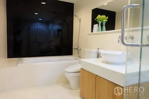 Condominium for rent in Khlong Toei, Bangkok - Modern condo bathroom with bathtub, vessel sink, glass shower and black accent wall in Khlong Toei