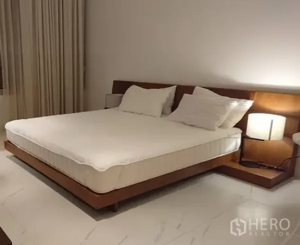 Condominium for rent in Pathum Wan, Bangkok - Spacious bedroom with king-size platform bed, wood headboard, bedside lamps and large floor tiles.
