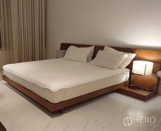 Condominium for rent in Pathum Wan, Bangkok - Spacious bedroom with king-size platform bed, wood headboard, bedside lamps and large floor tiles.