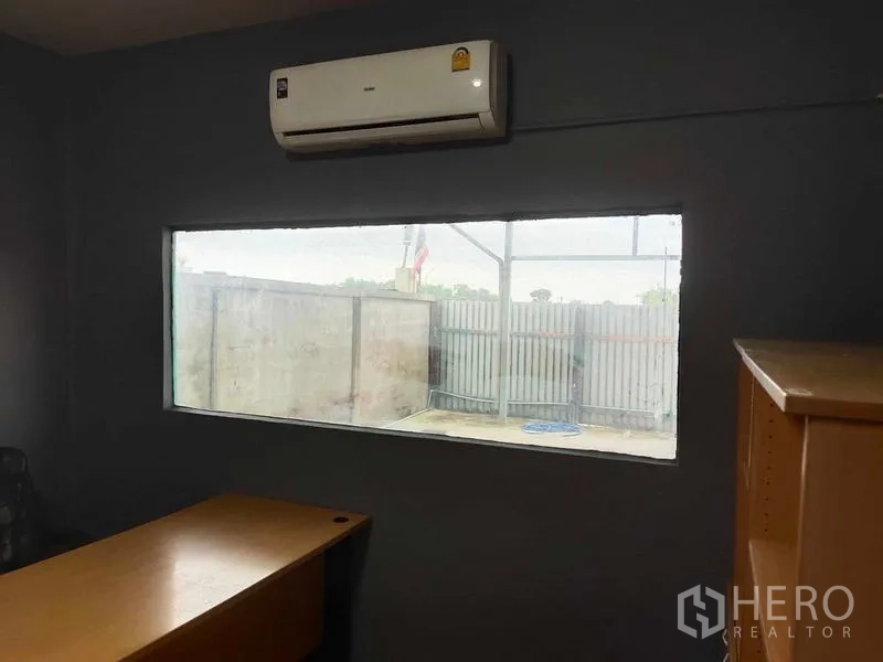 Warehouse for sale in Lam Luk Ka, Pathum Thani - Compact air-conditioned office with a wide window and wooden desk overlooking the yard.