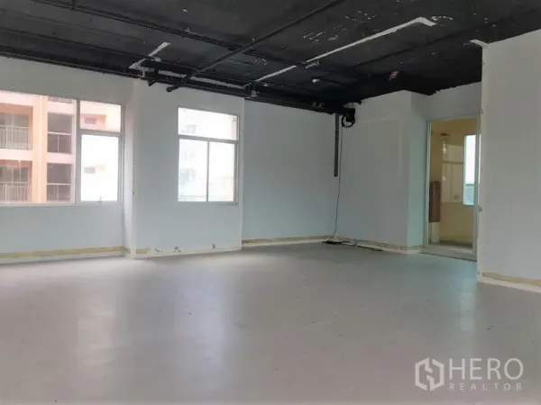 Office Space for rent in Phra Khanong, Bangkok - Spacious office shell with multiple windows, doorway to a utility room, and smooth light flooring near BTS access.