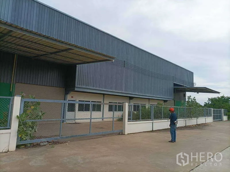 Factory for rent in Ban Phaeo, Samut Sakhon - Front facade of the warehouse showing gated entrance, canopy, and roller-shutter loading door.