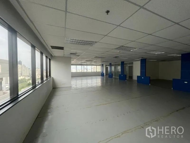 Office Space for rent - Large open workspace with full‑length windows, blue columns and skyline views.
