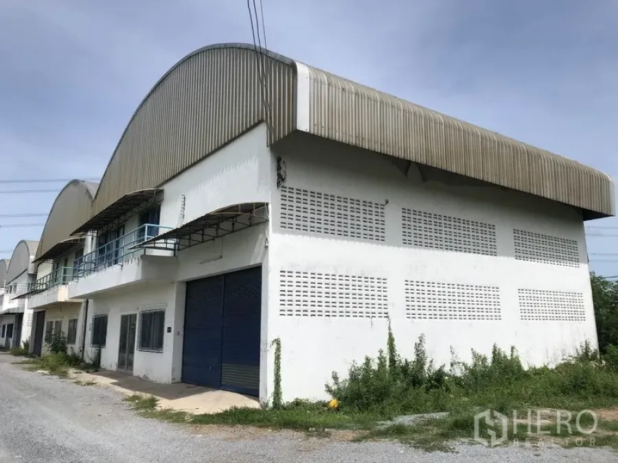 Warehouse for rent in Nonthaburi - End-unit warehouse exterior with curved metal roof and blue roller shutter in Sai Noi, Nonthaburi.