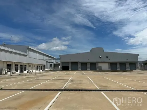 Factory for rent in Bang Sao Thong, Samut Prakan - Front elevation showing multiple roller-shutter loading bays and marked parking on a concrete apron.