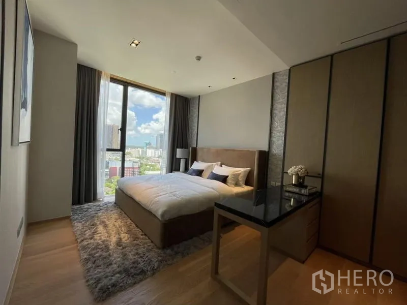 Condominium for rent in Khlong Toei, Bangkok - Bedroom with king bed, shag rug, built-in wardrobes, and tall window capturing a city view.