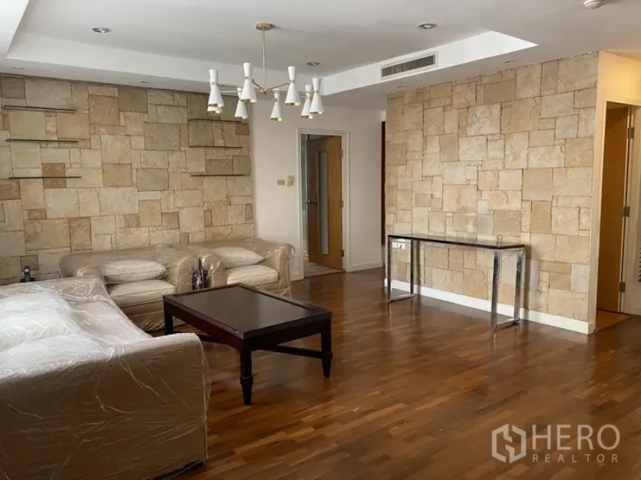 Condominium for rent or sale in Sathon, Bangkok - Spacious living room with stone accent walls, chandelier, sofas and coffee table on wooden flooring.