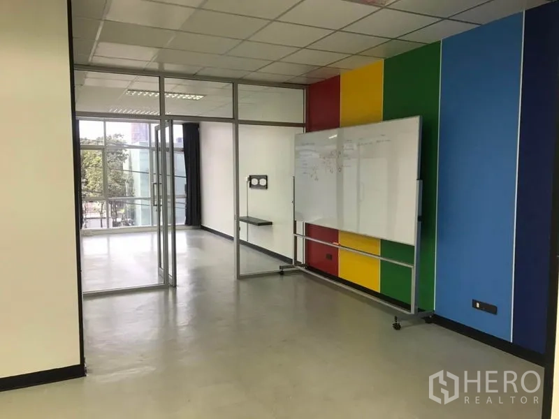 Office Space for rent in Khlong Toei, Bangkok - Meeting area with multicolor wall panels and a mobile whiteboard beside glass doors.