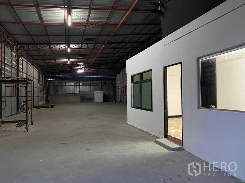 Warehouse for rent in Saphan Sung, Bangkok - Spacious warehouse hall featuring an internal office room and fluorescent lighting along the ceiling.