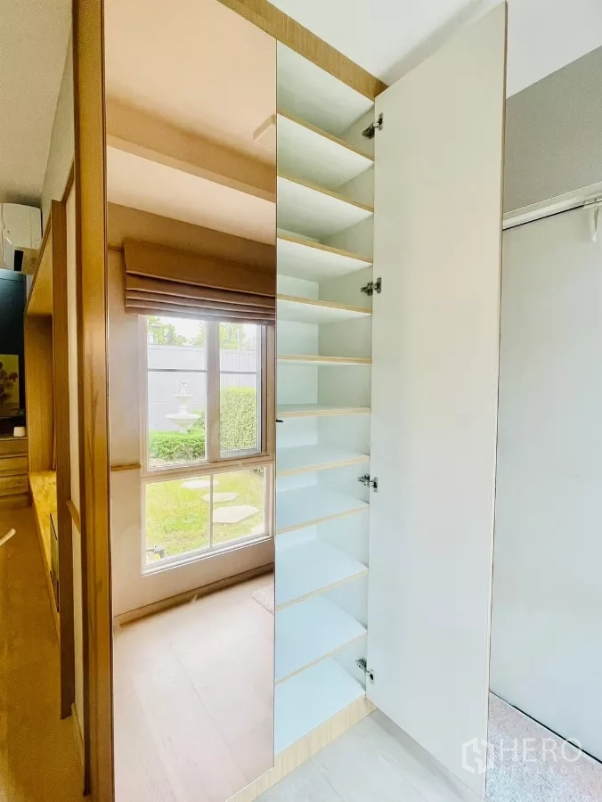 Detached House for rent in Prawet, Bangkok - Built-in storage cabinet with mirrored door and shelving by a garden-view window.