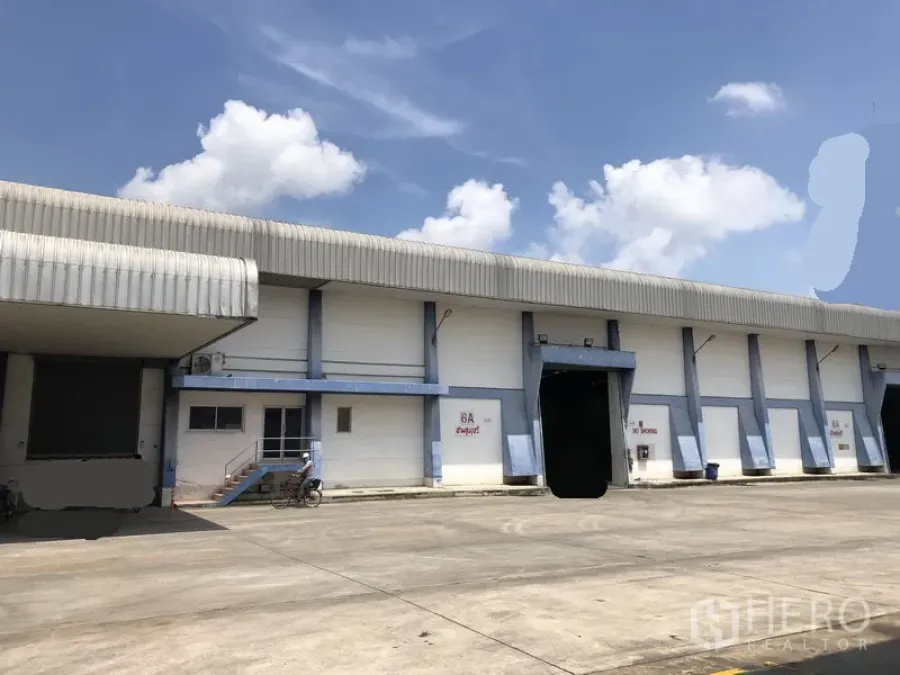 Warehouse for rent in Phra Nakhon Si Ayutthaya - Large warehouse exterior with covered loading bays and a wide truck yard under a blue sky.