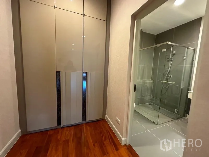 Detached House for rent or sale in Khan Na Yao, Bangkok - Hallway with glossy built-in wardrobe leading to a glass shower bathroom.