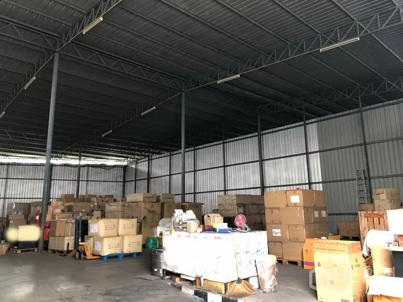 Warehouse for rent in Pak Kret, Nonthaburi - Open-plan storage area with high metal roof, shelving space and palletized goods.