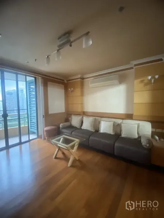 Condominium for rent in Pathum Wan, Bangkok - Bright living room with wood floors, long sofa, wall air-conditioning and sliding doors to a balcony with city views.