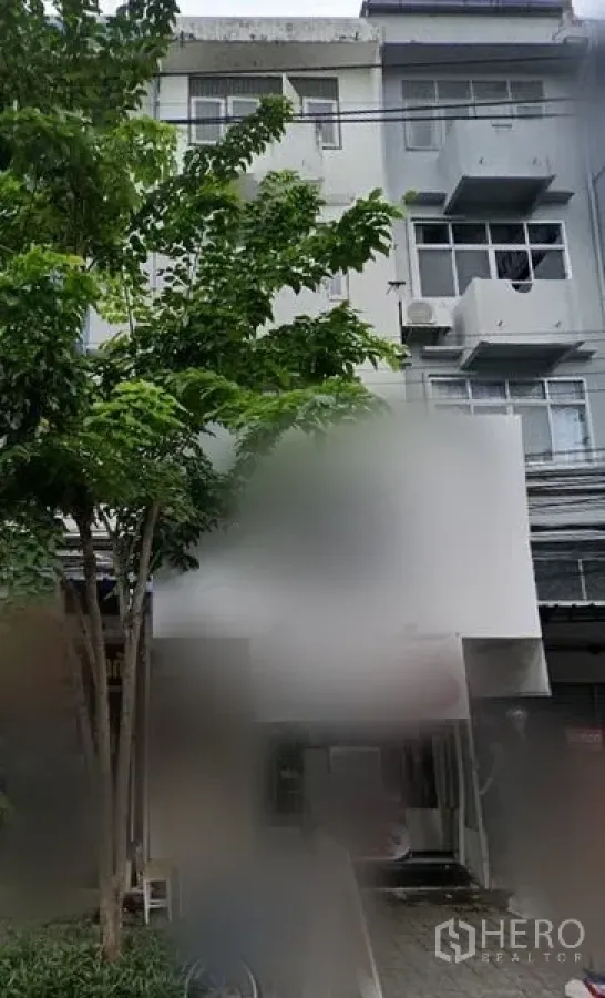 Shophouse for rent in Bang Na, Bangkok - Multi-storey shophouse exterior in Bang Na with balconies, air-conditioning units and large signboard, shaded by trees near BTS Udom Suk.
