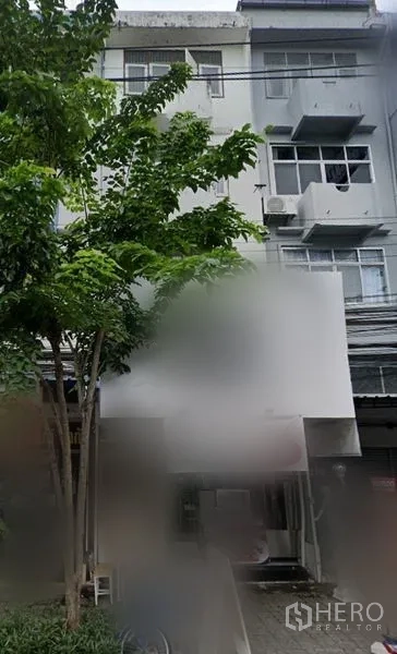 Shophouse for rent in Bang Na, Bangkok - Multi-storey shophouse exterior in Bang Na with balconies, air-conditioning units and large signboard, shaded by trees near BTS Udom Suk.
