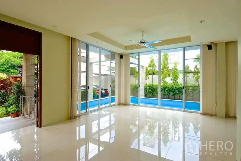 Detached House for rent in Watthana, Bangkok - Open, tiled living area with floor‑to‑ceiling windows overlooking the pool and garden.