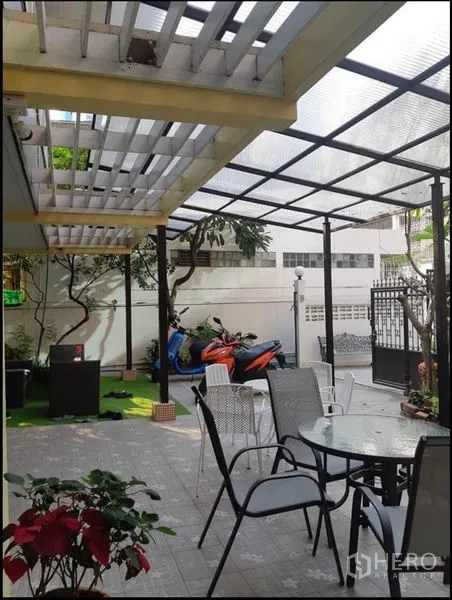 Detached House for rent in Watthana, Bangkok - Covered patio with transparent roof, outdoor dining set and scooters beside a small lawn.