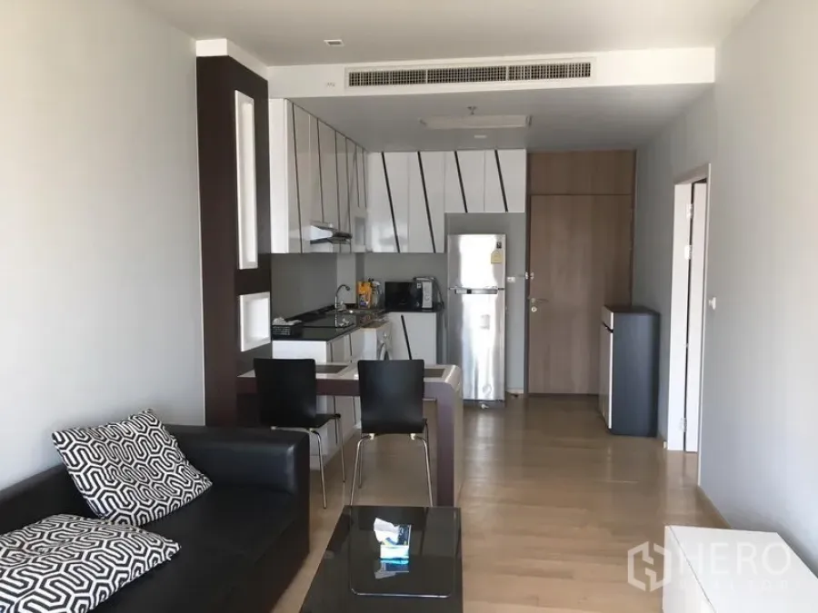 Condominium for rent in Bangkok - Open-plan living and kitchen with breakfast counter, dining chairs, sofa and natural wood floors.