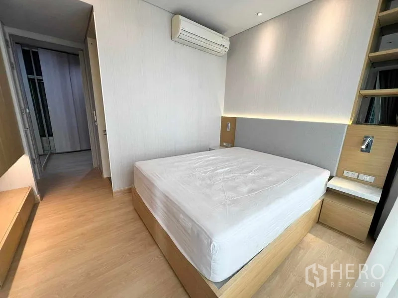 Condominium for rent or sale - Bright bedroom with platform bed, bedside tables, air conditioner, and soft wall lighting.