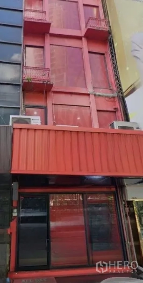 Shophouse for rent in Khlong Toei, Bangkok - Four-storey red shophouse facade with large streetfront windows and small balconies.