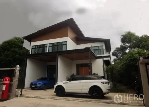 Detached House for sale in Pak Kret, Nonthaburi - Modern two-storey detached house with covered carport and large windows framed by greenery.