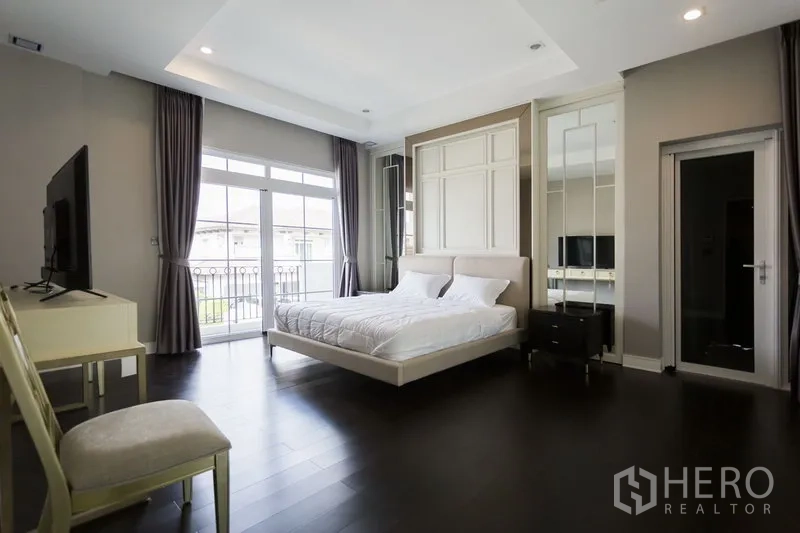 Detached House for rent in Mueang Samut Prakan, Samut Prakan - Master bedroom with balcony access, large windows, dark wood floors and built-in wardrobes.