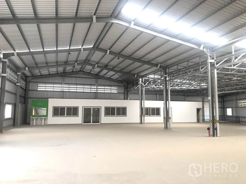 货栈 出租在Bang Yai, Nonthaburi - 库内带独立白色办公室模块，钢柱支撑与明亮屋面采光。