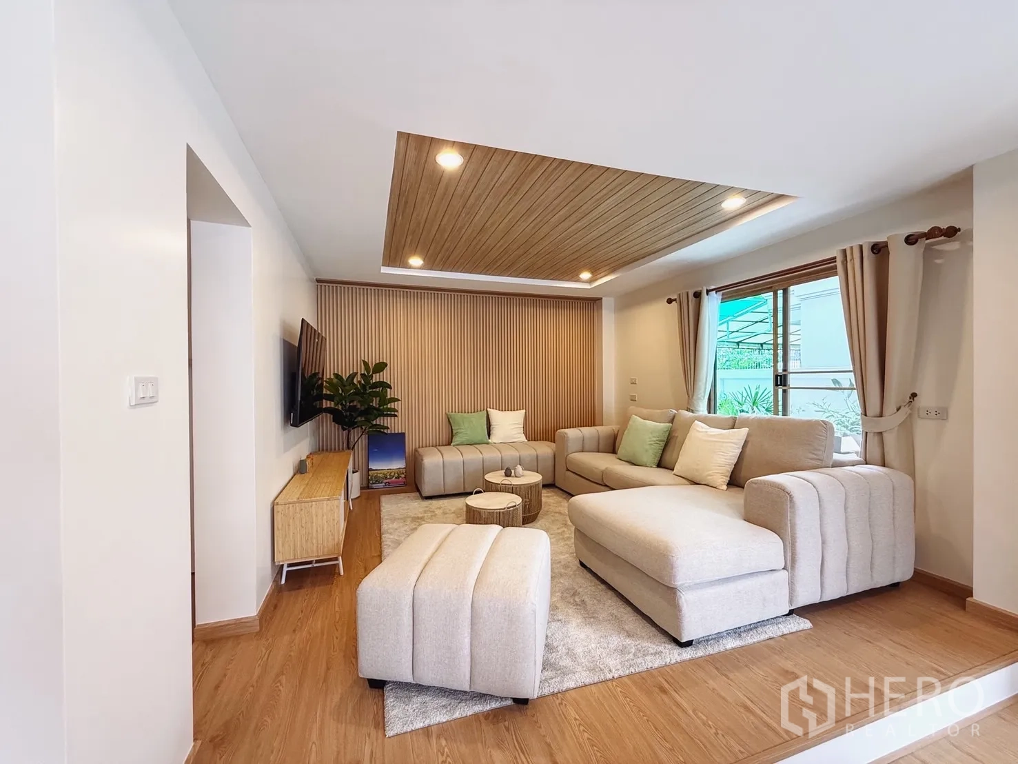 Detached House for sale in Suan Luang, Bangkok - Bright living room with beige sofas, wood accent ceiling and wall-mounted TV.