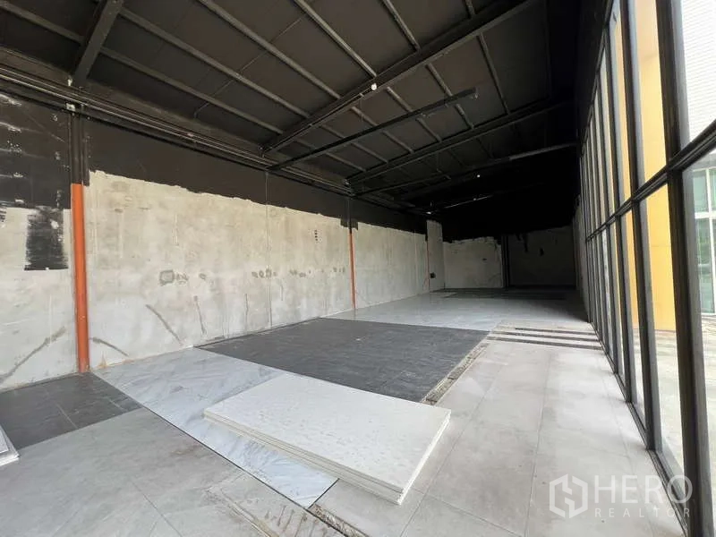 零售空间 出租在Bang Na, Bangkok - 开阔的零售室内，黑色高挑顶、清水墙与瓷砖地面，临整面落地玻璃门面。