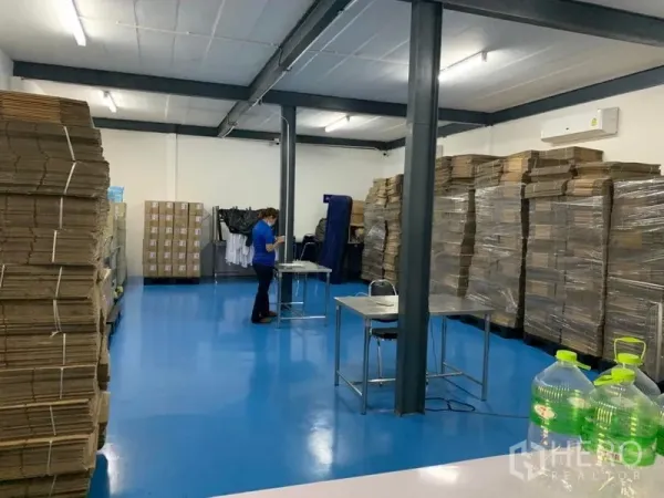 Warehouse for rent in Bang Kapi, Bangkok - Clean warehouse work area with blue epoxy flooring, steel columns, stacked cartons and wall-mounted air conditioners.