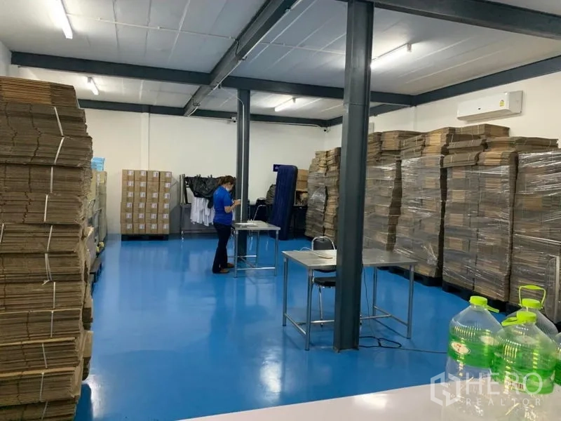 Warehouse for rent in Bang Kapi, Bangkok - Clean warehouse work area with blue epoxy flooring, steel columns, stacked cartons and wall-mounted air conditioners.