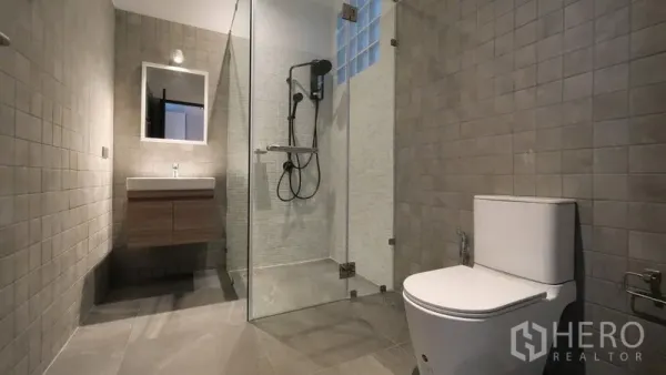 Townhouse for rent in Khlong Toei, Bangkok - Contemporary bathroom featuring a glass-enclosed shower, wall-mounted vanity, and gray tiles.