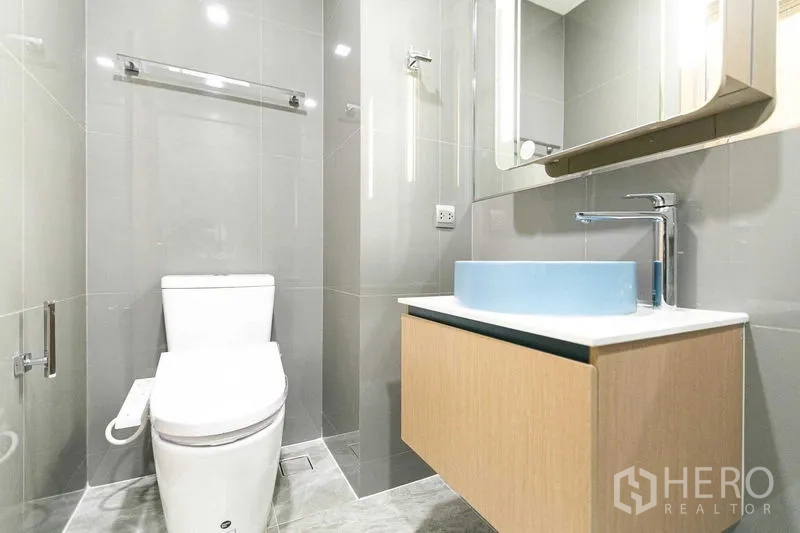 Condominium for sale in Watthana, Bangkok - Bathroom angle showing toilet, floating vanity with blue basin, and mirror cabinet.