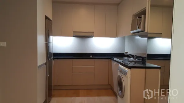 Condominium for rent in Khlong Toei, Bangkok - Modern U-shaped kitchen with built-in cabinets, stone countertops, fridge and washing machine.