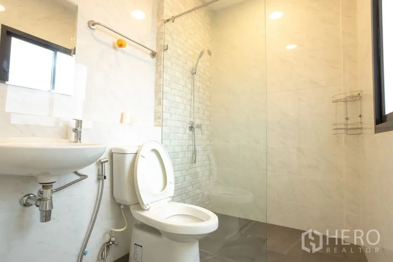 Home Office for rent in Bang Khen, Bangkok - Modern bathroom featuring glass-enclosed shower, window lighting and white wall tiles.