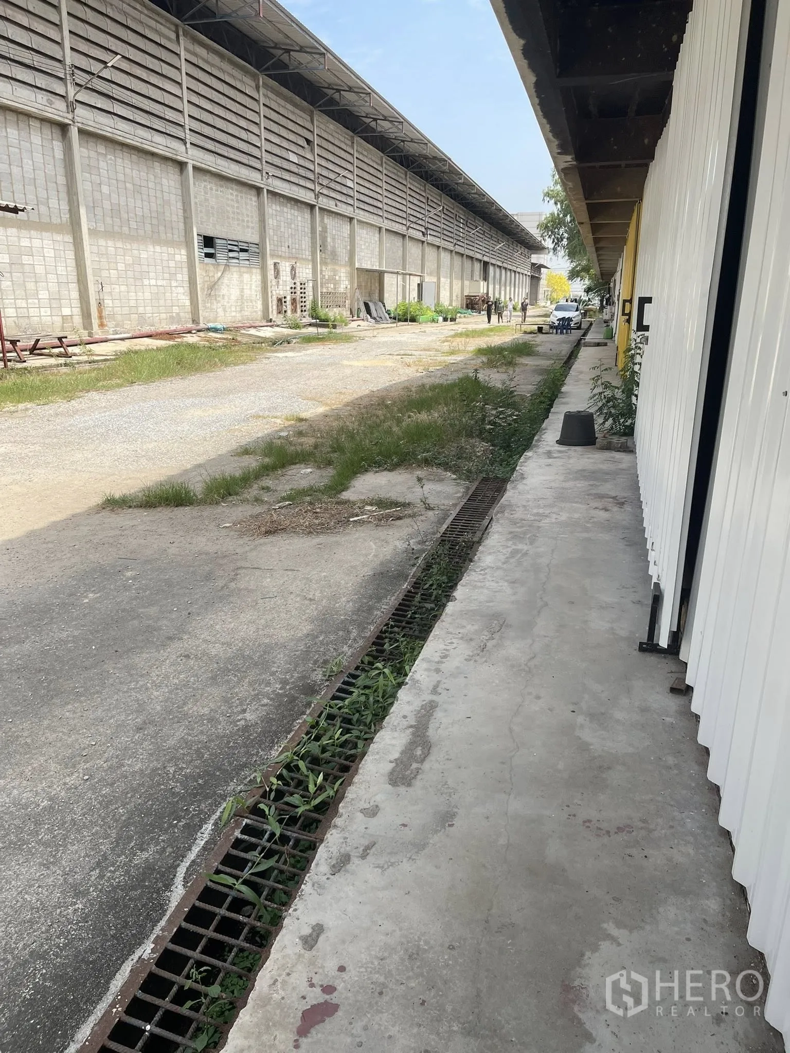 Factory for rent in Bang Bua Thong, Nonthaburi - Side walkway with metal drainage grates beside a long factory wall and service area.