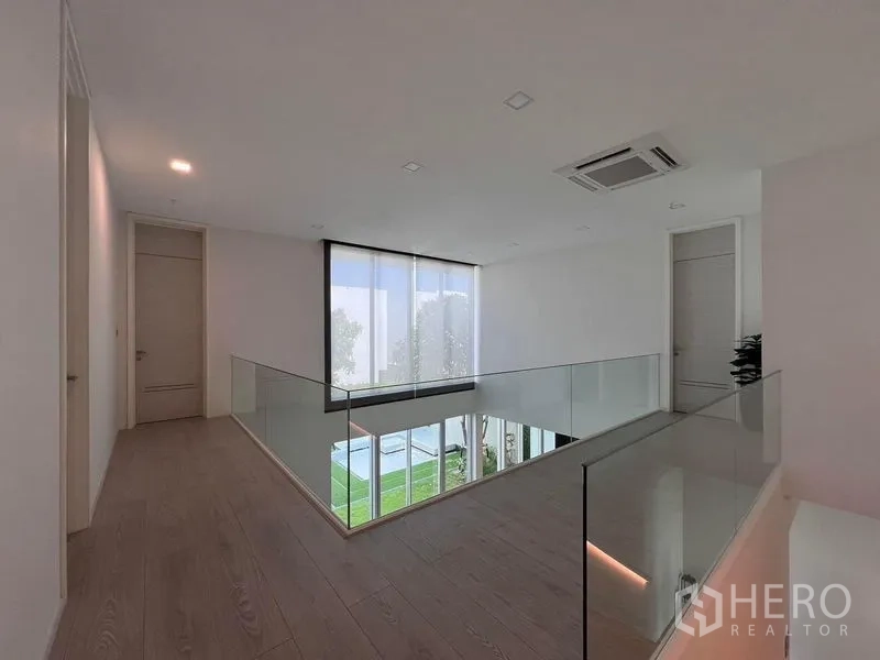 独立式住宅 出售在Samut Prakan - 二层走廊，玻璃护栏，可俯瞰客厅与花园。