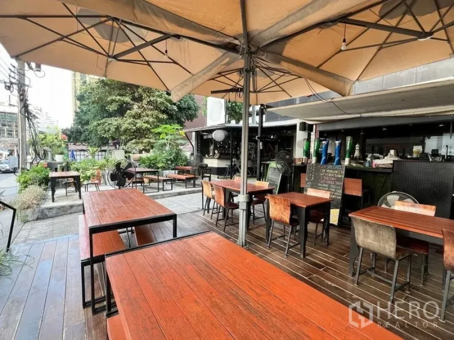 พื้นที่ขายปลีก ให้เช่าในWatthana, Bangkok - ลานนั่งกลางแจ้งหน้าร้าน โต๊ะไม้ ร่มขนาดใหญ่ และต้นไม้ริมถนน