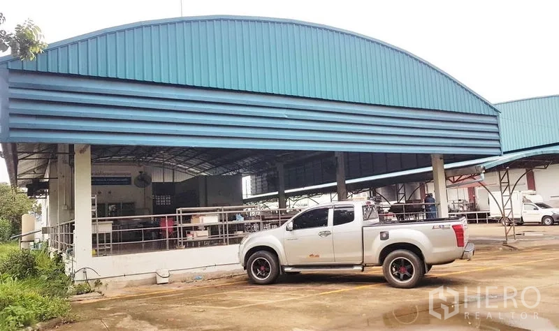 Factory for sale in Lam Luk Ka, Pathum Thani - Angle of curved‑roof shed and marked parking bays beside the main factory building.