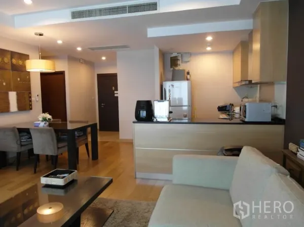 Condominium for rent or sale in Sathon, Bangkok - Bright lounge facing a built-in kitchen with light wood cabinets, dining table and entry hallway.