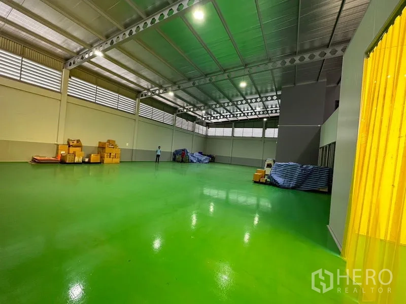 Factory for rent or sale in Lam Luk Ka, Pathum Thani - Large warehouse zone with yellow PVC strip curtain, high ceiling and polished green floor.