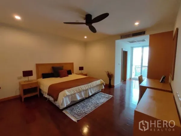 Condominium for rent in Khlong Toei, Bangkok - Primary bedroom with king bed, ceiling fan, wood floors and balcony access.