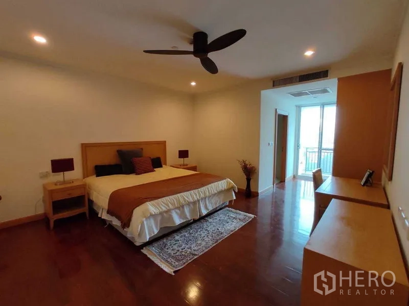 Condominium for rent in Khlong Toei, Bangkok - Primary bedroom with king bed, ceiling fan, wood floors and balcony access.