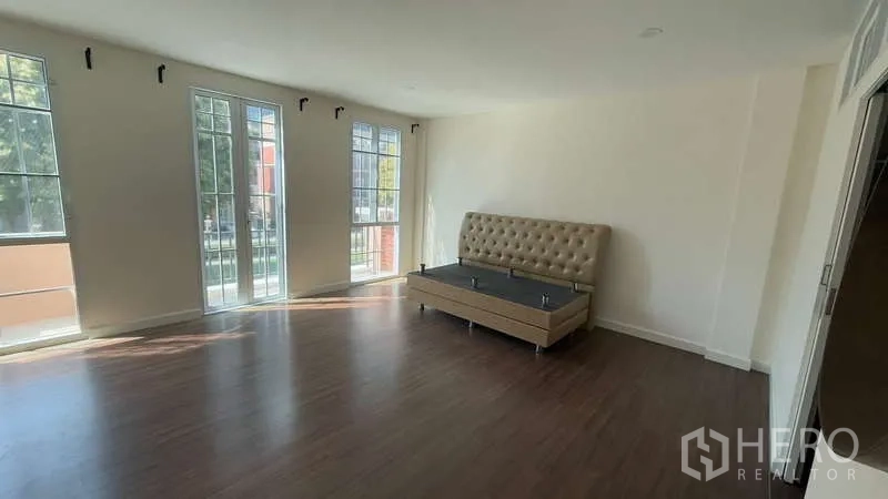 Townhouse for sale in Watthana, Bangkok - Large master bedroom with floor-to-ceiling windows and wood flooring.