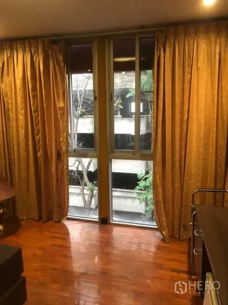 Shophouse for rent in Bang Rak, Bangkok - Tall window with gold curtains and city view beside polished wood floor.
